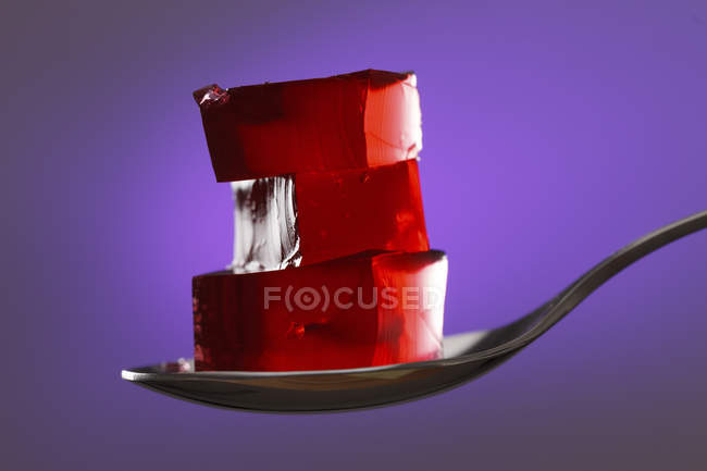 Cubi di gelatina rossa su cucchiaio su sfondo viola . — Foto stock