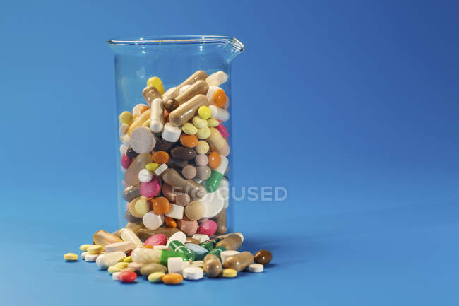 Flacon en verre avec des pilules colorées de différentes formes sur fond bleu . — Photo de stock
