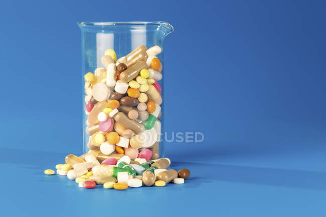 Pallone di vetro con pillole colorate di varie forme su sfondo blu . — Foto stock