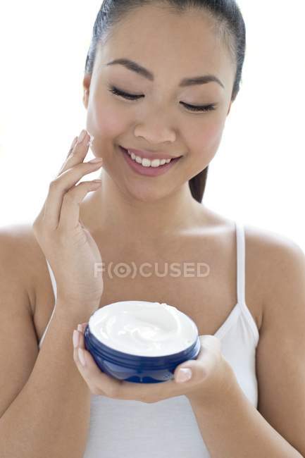 Asiatique jeune adulte appliquant crème visage sur fond blanc . — Photo de stock