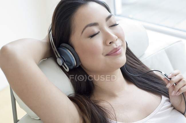 Женщина в кресле в наушниках и слушает музыку с закрытыми глазами . — стоковое фото