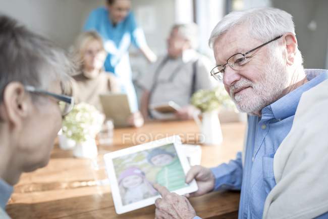 Senior adults looking at photo on digital tablet in care home. — Stock Photo