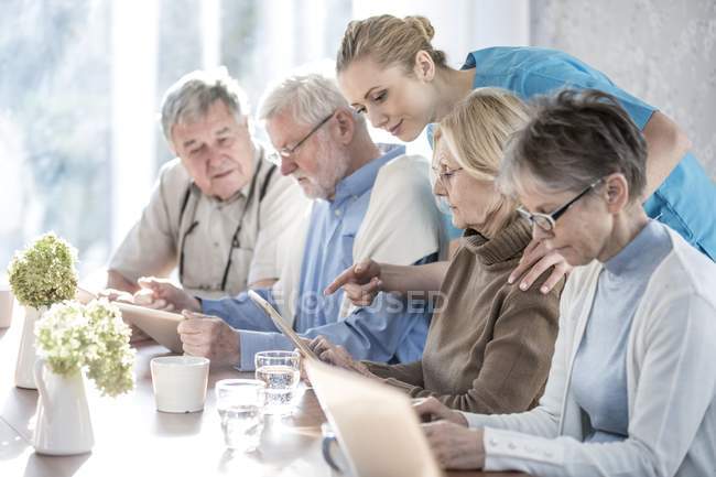 Senior adults in care home using tablet computers with care worker. — Stock Photo