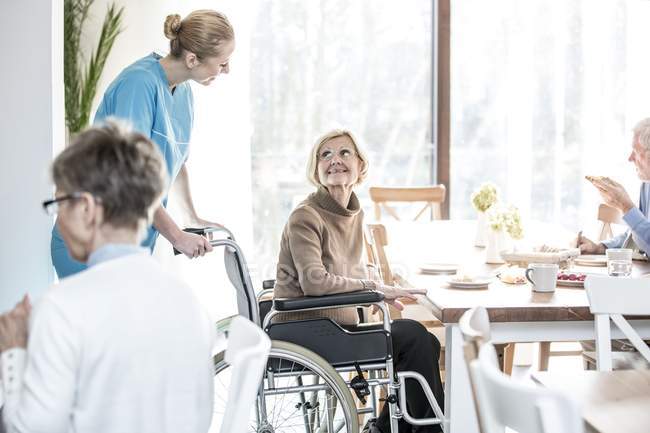 Mujer mayor en silla de ruedas sonriendo y mirando al trabajador del cuidado
. - foto de stock