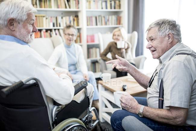 Старший в инвалидной коляске разговаривает с друзьями в доме престарелых . — стоковое фото