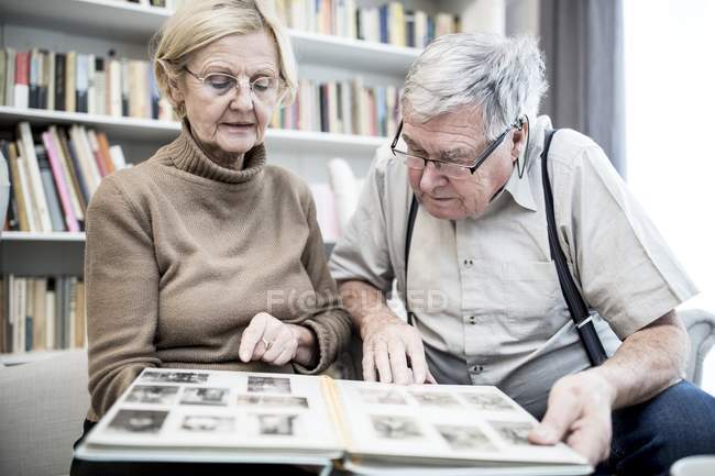 Seniorenpaar betrachtet Fotoalbum im Wohnzimmer. — Stockfoto