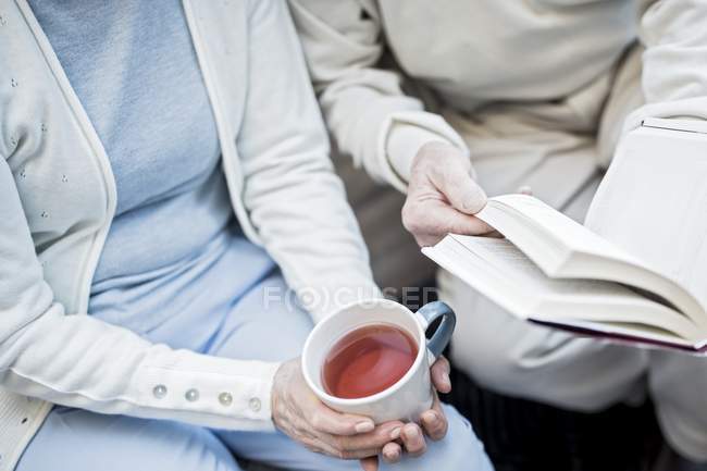 Vue recadrée de la femme avec tasse de thé avec l'homme tenant livre
. — Photo de stock