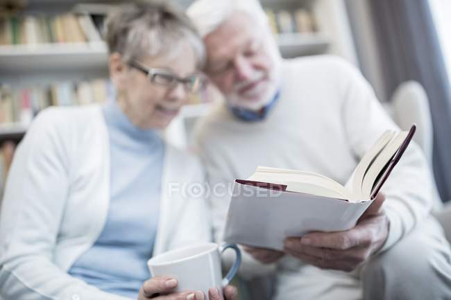 Senior couple reading book and holding cup of tea together. — Stock Photo