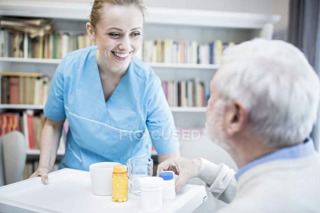 Догляд працівник виступає старший чоловік медицина пляшок на лоток. — стокове фото