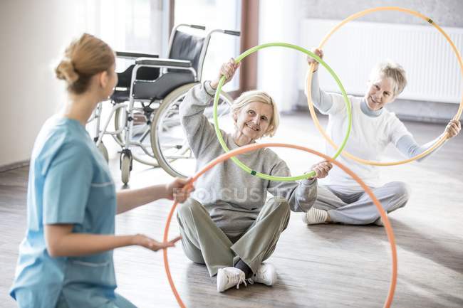 Fisioterapista con donne anziane che praticano con cerchi di plastica . — Foto stock