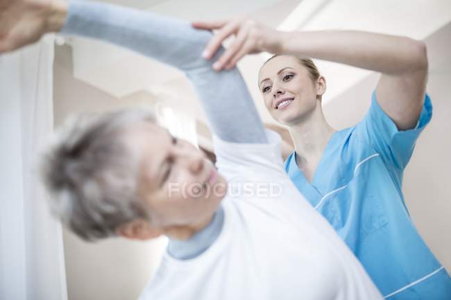 Donna anziana che si allunga con fisioterapista aiutando, vista a basso angolo
. — Foto stock