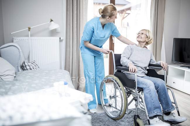 Donna anziana sulla sedia a rotelle che parla con il lavoratore in casa di cura . — Foto stock