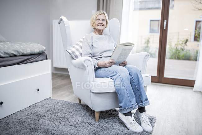 Seniorin sitzt mit Magazin im Sessel in Pflegeheim. — Stockfoto