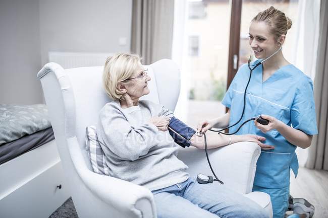 Krankenschwester lächelt und nimmt Blutdruck von Seniorin. — Stockfoto