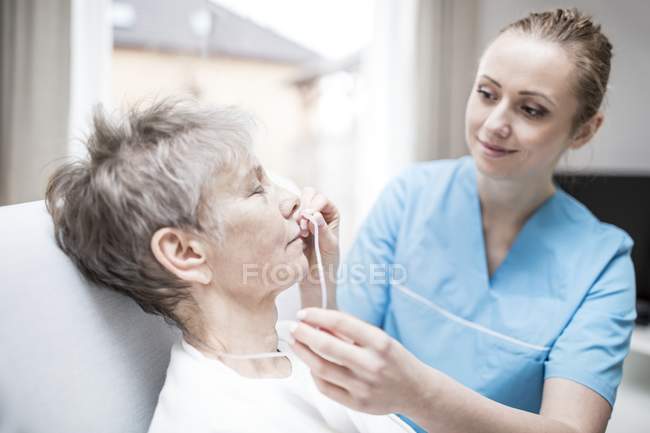 Enfermera insertando cánula nasal en mujer mayor . - foto de stock