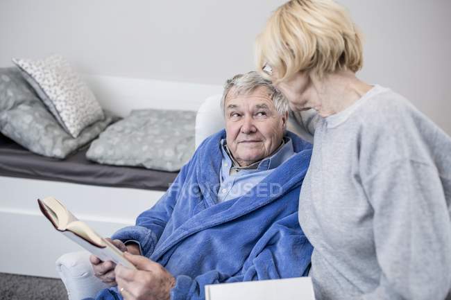 Casal sênior olhando uns para os outros enquanto lia livros em casa de cuidados . — Fotografia de Stock
