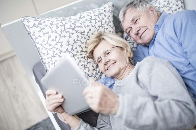 Seniorenpaar legt sich ins Bett und schaut digitales Tablet. — Stockfoto