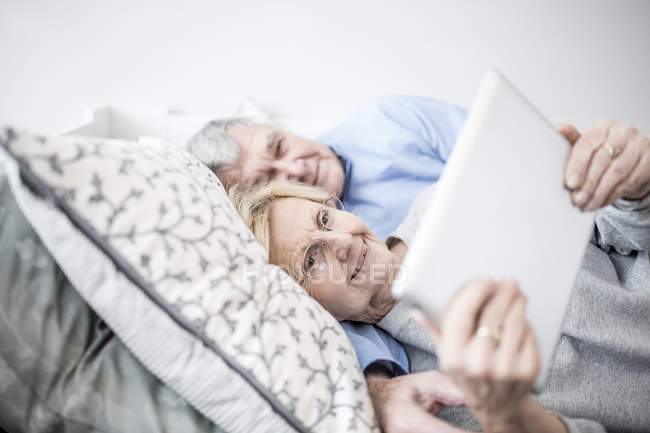 Старшая пара лежит в постели и смотрит цифровой планшет . — стоковое фото