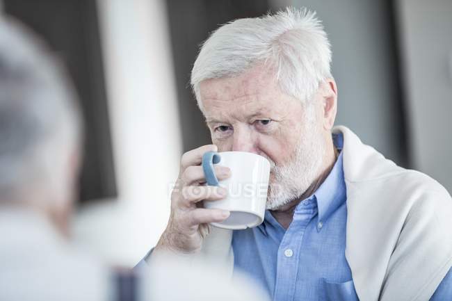 Senior man drinking cup of tea while talking with friend. — Stock Photo