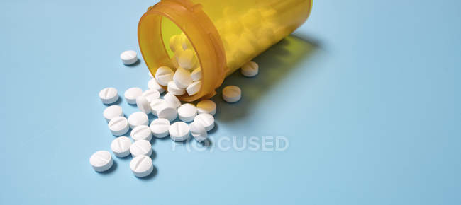 Nahaufnahme weißer Tabletten, die aus einem gelben Behälter auf blauem Hintergrund austreten. — Stockfoto