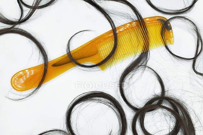 Yellow comb and scattered black hair on white background. — Stock Photo