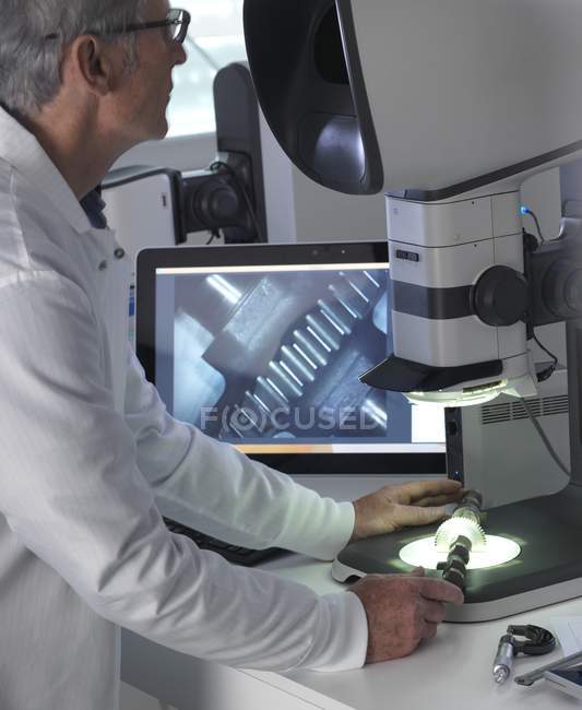 Male engineer using stereo microscope for inspecting manufactured component during quality control process. — Stock Photo