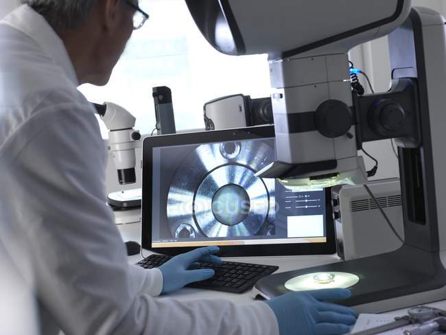 Ingegnere maschio che utilizza lo stereomicroscopio per ispezionare i componenti fabbricati durante il processo di controllo della qualità . — Foto stock