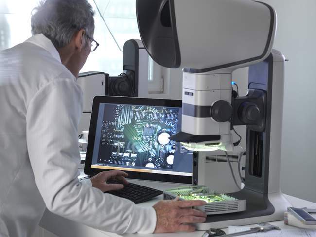 Engineer using stereo microscope for inspecting printed circuit board during quality control process. — Stock Photo