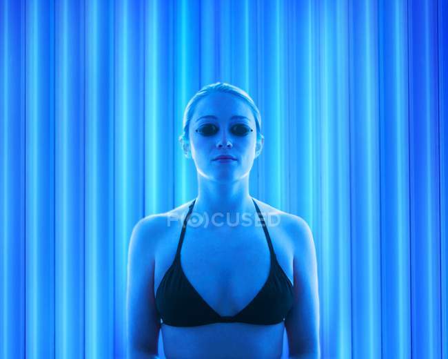 Young woman wearing protective goggles in tanning booth. — Stock Photo