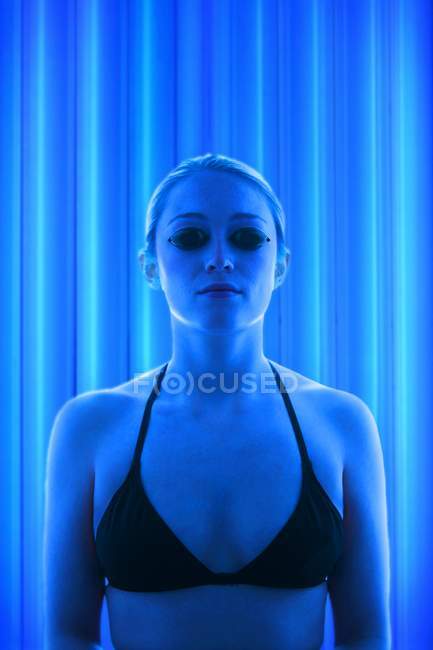 Young woman wearing protective goggles in tanning booth. — Stock Photo