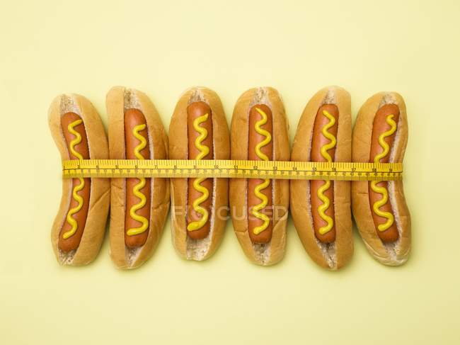 Fita de medição em torno de cachorros-quentes no fundo amarelo . — Fotografia de Stock