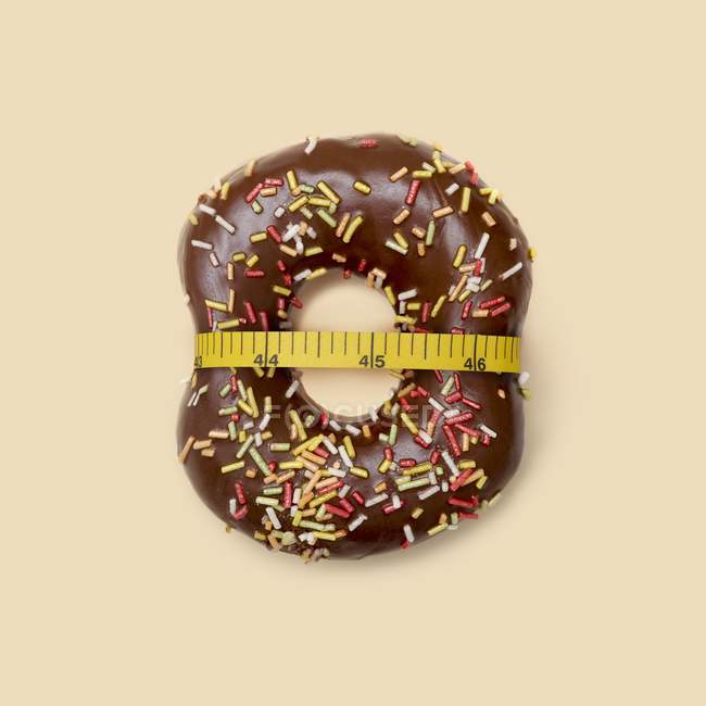 Chocolate doughnut with sugar strands squeezed by tape measure, studio shot. — Stock Photo