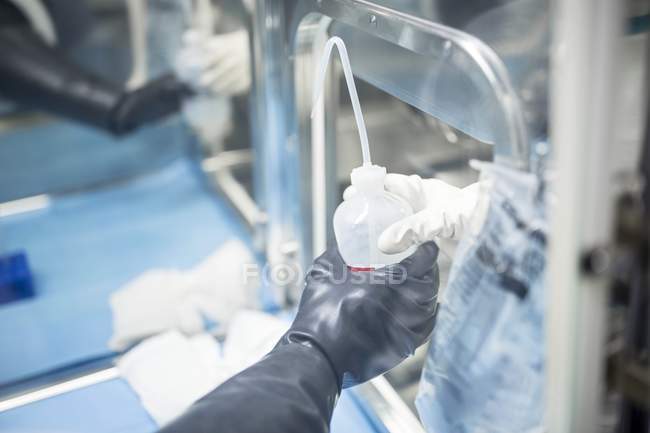 Cropped view of technicians passing bottle of solution in sterile laboratory. — Stock Photo