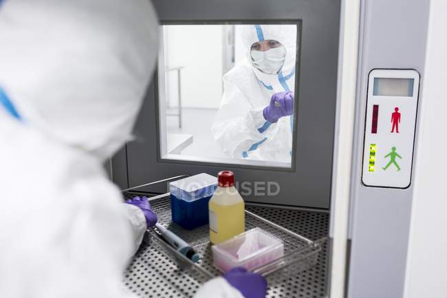 Technician collecting equipment from transfer hatch in sterile laboratory. — Stock Photo