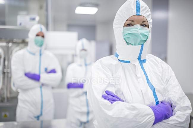 Lab technician in protective clothing with colleagues in sterile laboratory environment. — Stock Photo