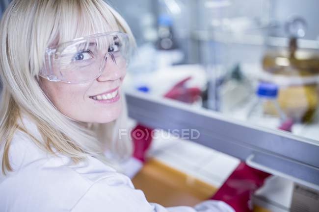 Técnico de laboratório em luvas grossas e óculos de segurança usando capa de fluxo laminar enquanto trabalha com produtos químicos perigosos . — Fotografia de Stock