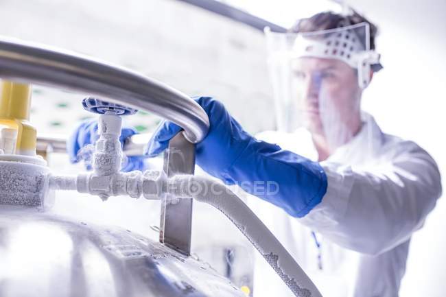 Male technician with face shield closing cryostorage. — Stock Photo