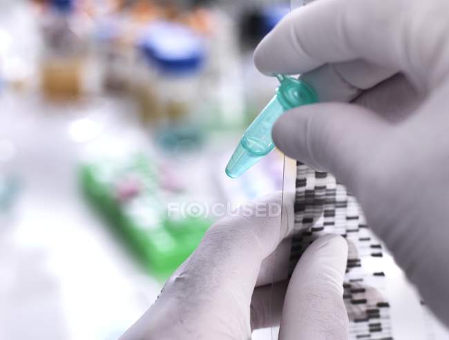 Scientist holding DNA sample in tube with autoradiograph on DNA gel. — Stock Photo