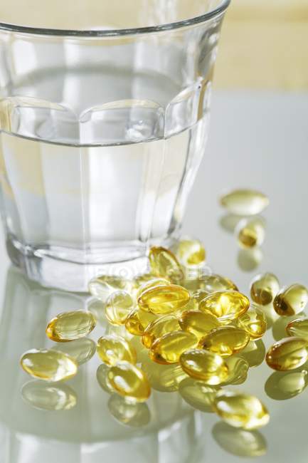Evening primrose oil capsules in pile next to transparent glass of water. — Stock Photo