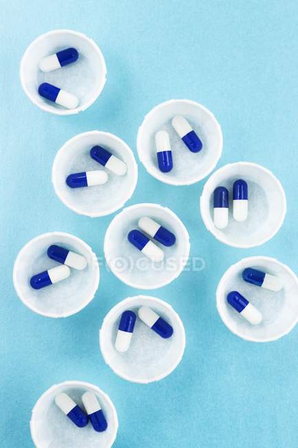 Vue du dessus des pots à pharmacie en papier avec capsules bleues et blanches . — Photo de stock