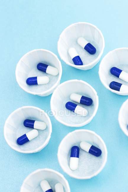 Draufsicht auf Papier-Medikamententöpfe mit blauen und weißen Kapseln. — Stockfoto