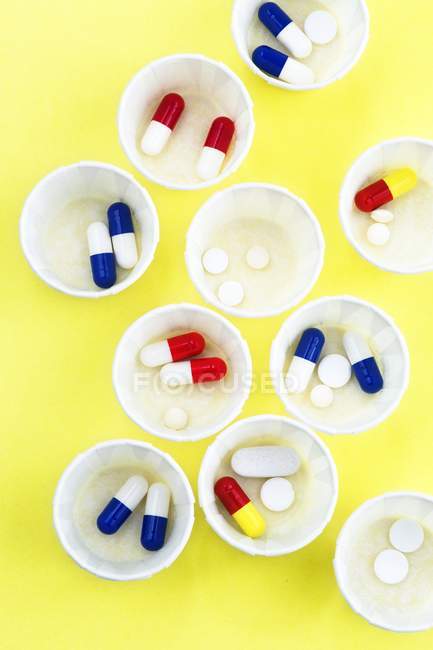 Vista dall'alto di vasi di medicina di carta con varie pillole su sfondo giallo
. — Foto stock