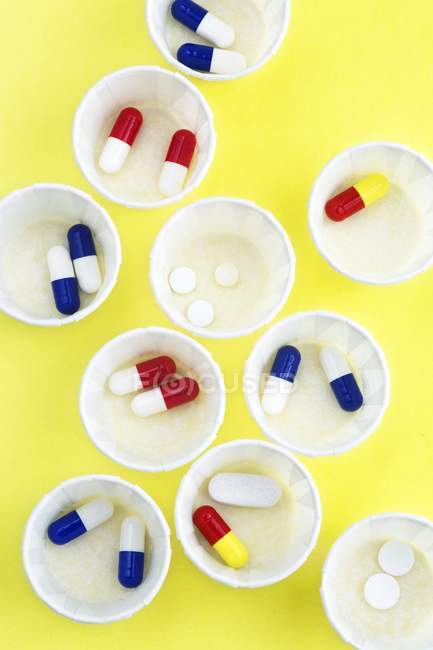 Vue du dessus des pots de médecine en papier avec diverses pilules sur fond jaune . — Photo de stock