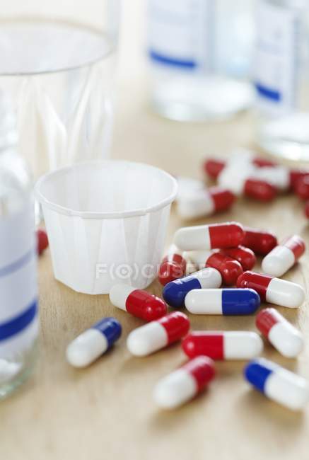 Cápsulas de drogas vermelhas e brancas e azuis e brancas e xícara de papel na mesa de madeira . — Fotografia de Stock