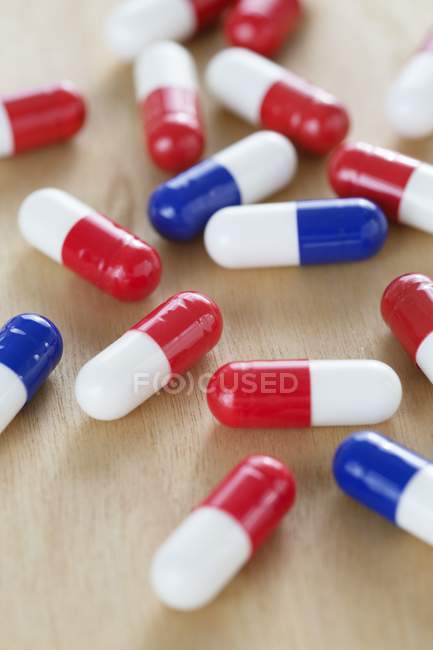 Capsule di droga rosse e bianche e blu e bianche sul tavolo di legno . — Foto stock