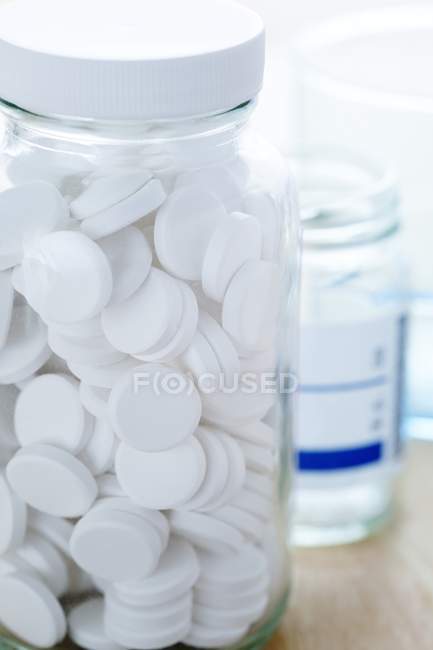Weiße runde Pillen in Glasflasche auf dem Tisch. — Stockfoto