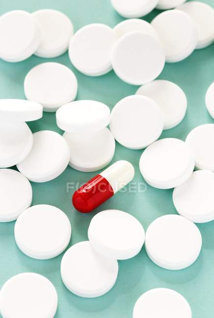 Круглі білий таблетки оточують овальні червоного та білого капсули. — стокове фото