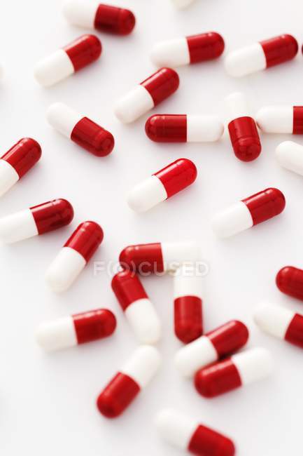 Красно-белые капсулы препарата разбросаны на белом фоне . — стоковое фото