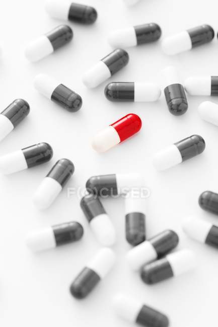 Capsule rouge et blanche entourée de pilules noires et blanches éparpillées sur fond blanc
. — Photo de stock