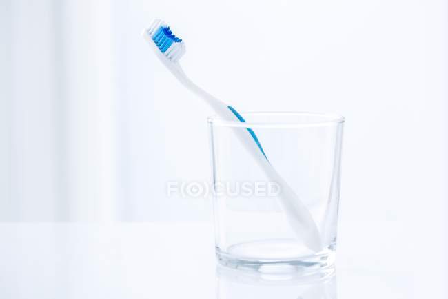Cepillo de dientes azul en vidrio sobre fondo liso . - foto de stock
